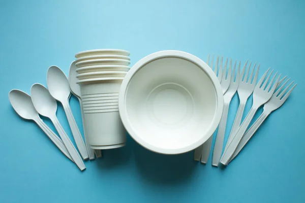 Biodegradable disposable tableware: plates, glasses and spoons with forks on a blue background close-up copy space. Trend: ecology.