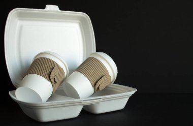 Plastik bir yiyecek kabının içinde, siyah bir arka plan ve kopyalamak için kullanılan iki adet tek kullanımlık bardak. Kavram atığı yok etme