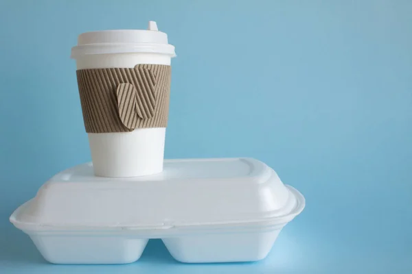 A disposable coffee Cup and a white container with food close-up on a blue background and space for copying. The concept of food delivery takeaway