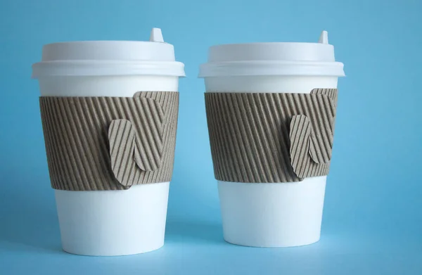 Two white disposable coffee cups close up on a blue background and a copy space