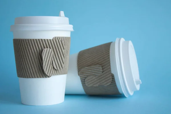 Two white disposable coffee cups close up on a blue background and a copy space