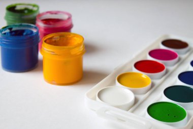 Plastik kavanozlarda çok renkli guaj, beyaz arka planda suluboya boyalar ve sanat fırçaları.