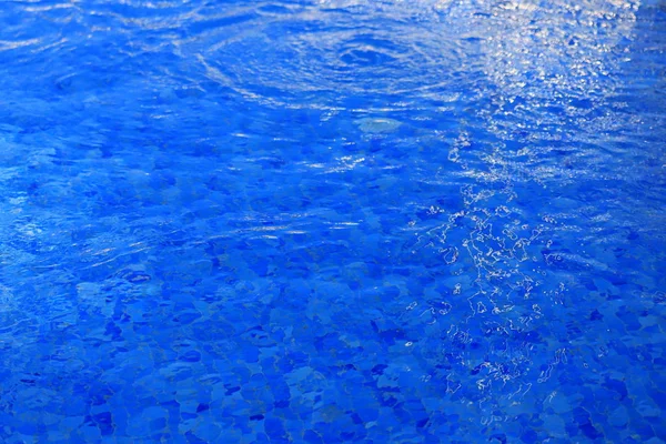 De achtergrond is blauw helder water in het zwembad met golven en lichtinval — Stockfoto