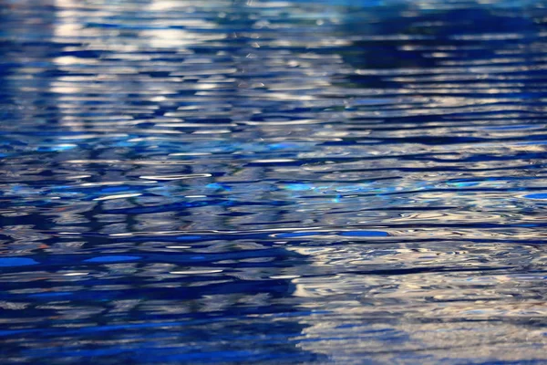 De achtergrond is blauw helder water in het zwembad met golven en lichtinval — Stockfoto