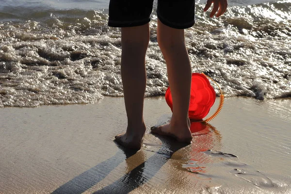 Uma criança na praia brinca com água com um balde de brinquedo — Fotografia de Stock