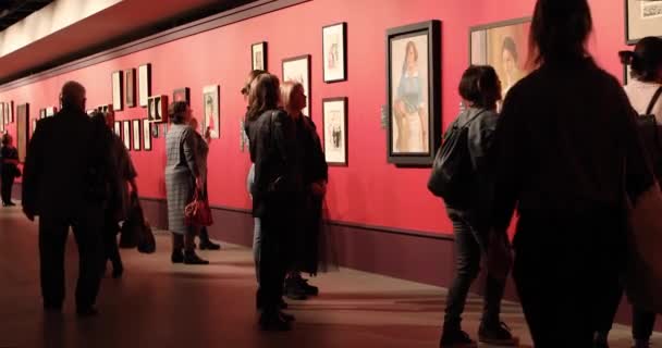 Lidé procházejí galerií umění, dívají se na obrazy a diskutují o nich — Stock video