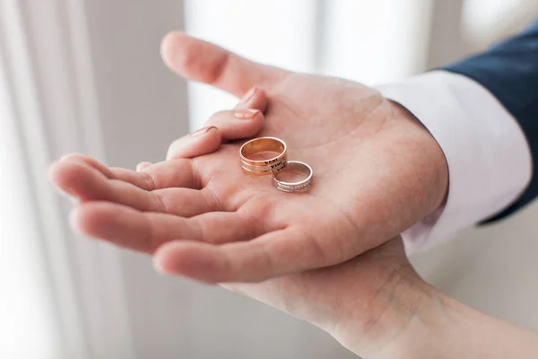 Newlywed Couple Showing In Their Hands Two Wedding Rings. Groom Holding On The Palm Pair Of Bridal Rings with a Latin phrase inscription: 