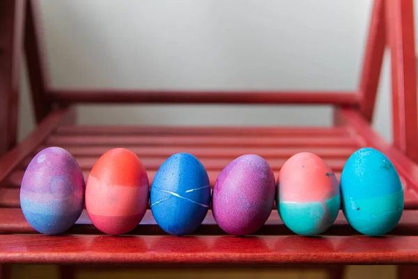 Colored easter eggs in a ceramic bowl on red background. Bright Colorful festive eggs abstractly painted blue, pink, green and purple.