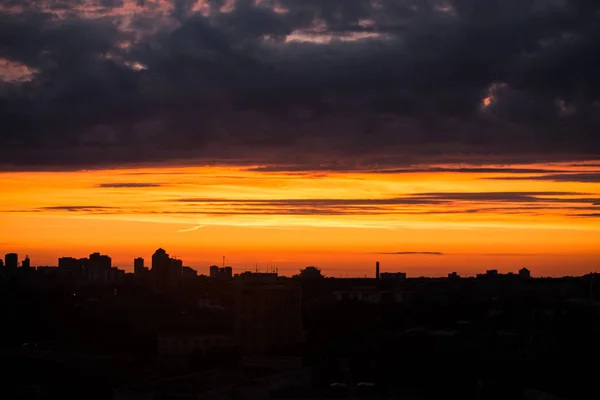 Şehri ele bulutlar ile sıcak gün batımı sırasında yükselen güneş