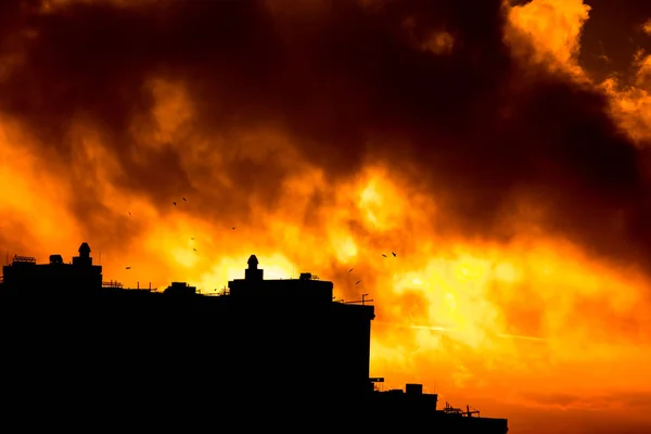 Şehri ele bulutlar ile sıcak gün batımı sırasında yükselen güneş