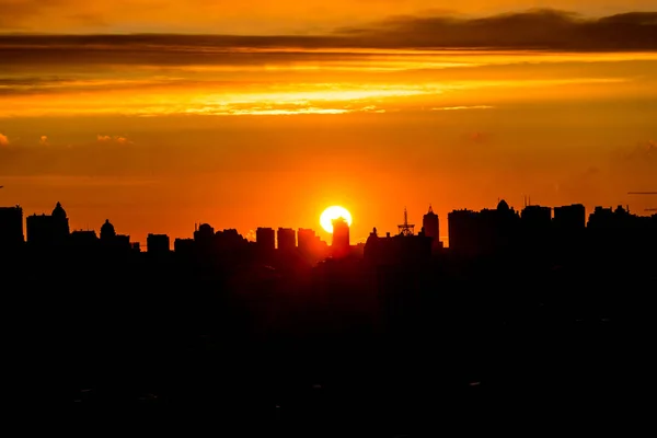 Şehri ele bulutlar ile sıcak gün batımı sırasında yükselen güneş