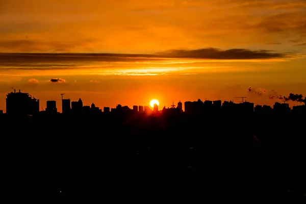 Şehri ele bulutlar ile sıcak gün batımı sırasında yükselen güneş