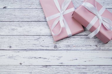 Beyaz ahşap yüzeyde duran iki pembe ambalajlı hediye ve fotokopi alanı.