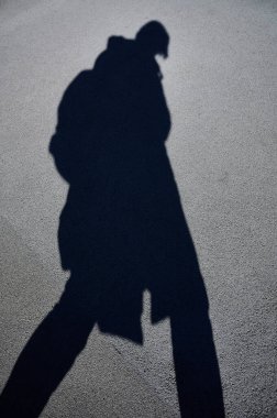Gri asfaltta yürüyen bir kadının gölgesi