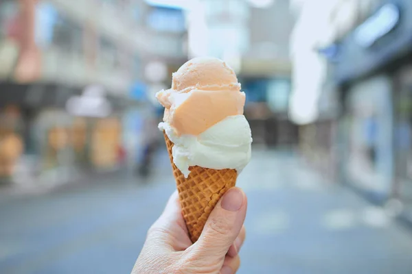 ice cream cone with two balls of ice cream in front of shops in a city center