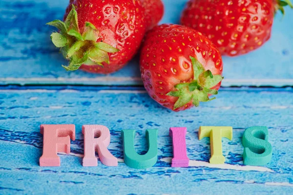 青い背景に新鮮なイチゴの横に色のついた木製の文字が敷かれた果物 — ストック写真