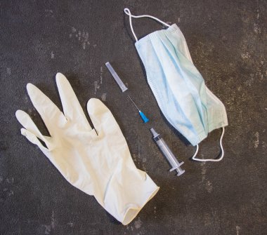 Tıbbi maske, tıbbi eldivenler ve siyah arka planda bir şırınga. Coronavirüs ve grip ilacı.