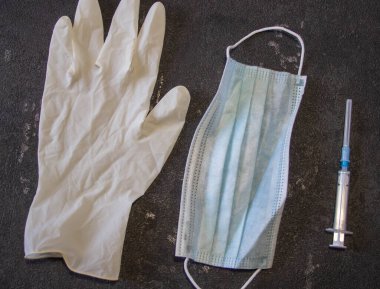 Coronavirus ve grip kontrolü. Tıbbi maske, siyah arka planda iğne ve lastik eldivenli şırınga.. 