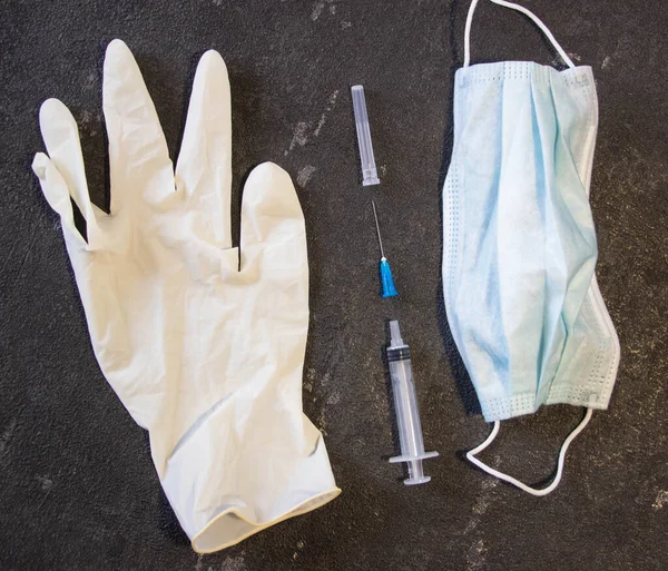 Medical mask, medical gloves and a syringe on a black background. Coronavirus and flu remedy.