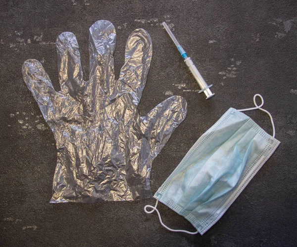 Transparent gloves, a medical mask and a medical syringe on a black background. Coronavirus and flu remedy.