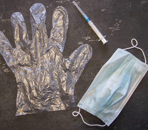 Transparent gloves, a medical mask and a medical syringe on a black background. Coronavirus and flu remedy.