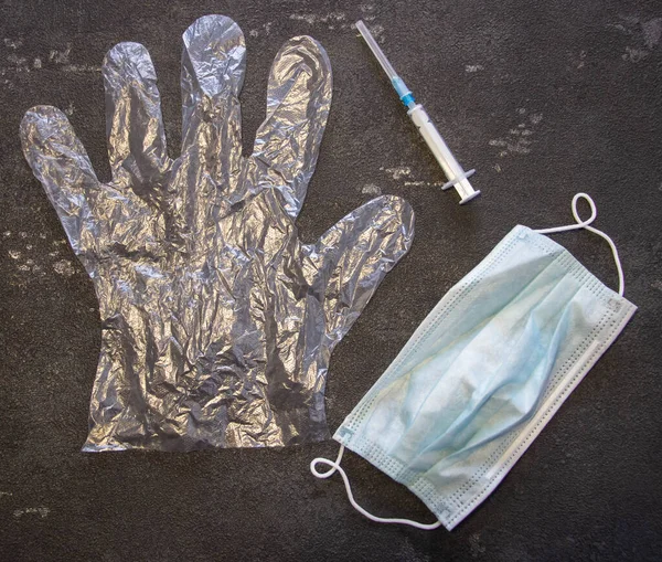 Transparent gloves, a medical mask and a medical syringe on a black background. Coronavirus and flu remedy.