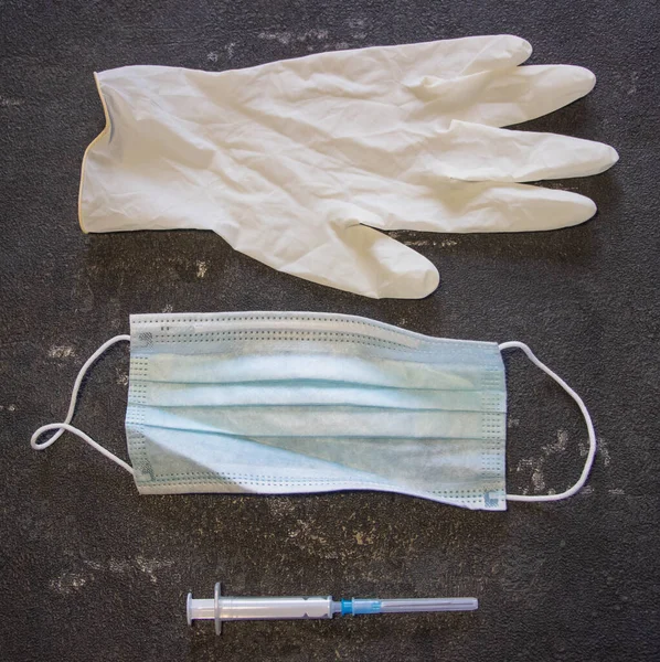 Coronavirus ve grip kontrolü. Tıbbi maske, siyah arka planda iğne ve lastik eldivenli şırınga.. 