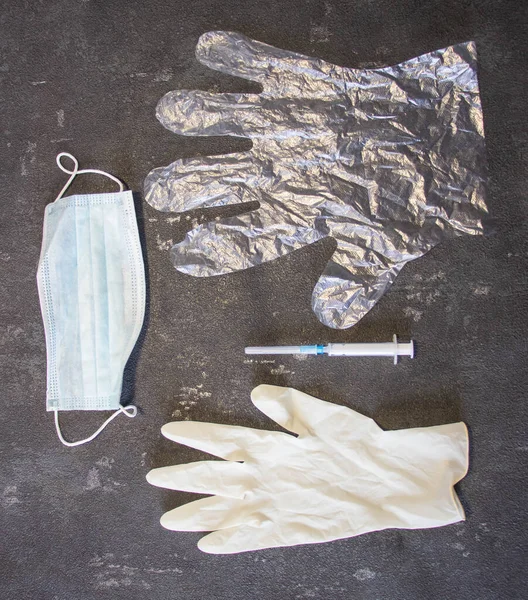 Transparent gloves, syringe, medical mask and rubber medical gloves on a black background. Coronavirus and flu remedy.