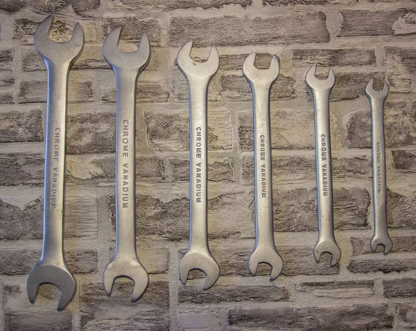 Set of open-end wrenches under the nuts on a brick wall background.