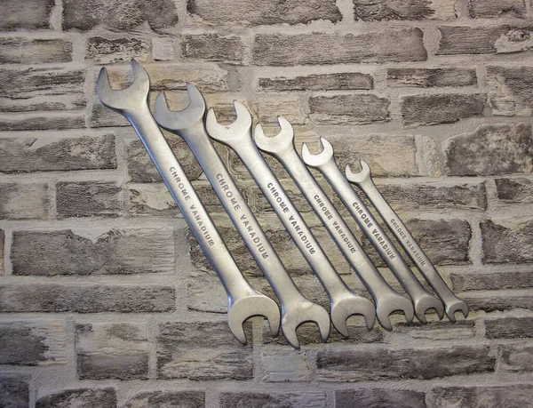 Set of open-end wrenches under the nuts on a brick wall background.