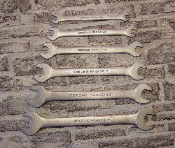 Set of open-end wrenches under the nuts on a brick wall background.