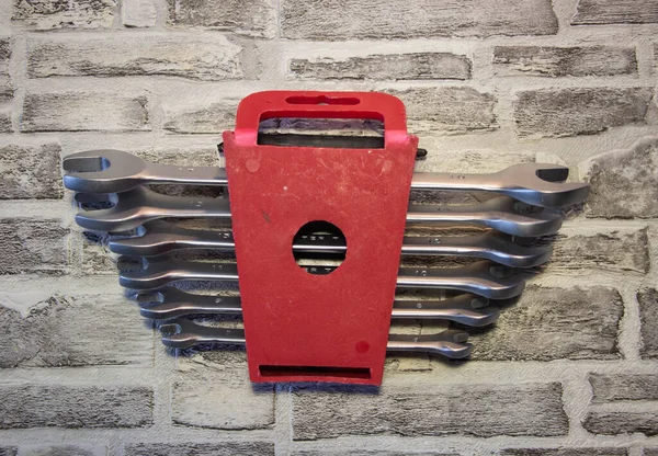 Set of open-end wrenches under the nuts on a brick wall background.