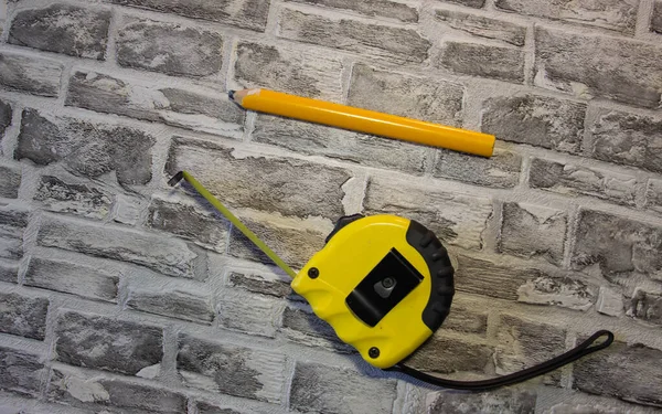 Yellow construction tape measure and yellow pencil on brick backgroun