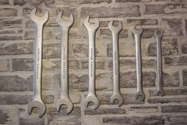 Set of open-end wrenches under the nuts on a brick wall background.