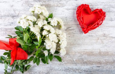 Kırmızı kurdeleli beyaz güller ve fotoğraf ya da yazı için rattan kalp çerçevesi beyaz doku tahtasına konur. Sevgililer Günü için arka plan, düğün, aşk. Metin için boşluk, üst görünüm, kopyalama alanı, düz alan.