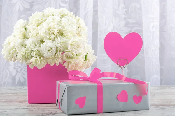 White roses in a pink square box, gift box and a symbol of the heart for the inscription close-up. Valentine's day, wedding, declaration of love. Space for text, front view, copy space.