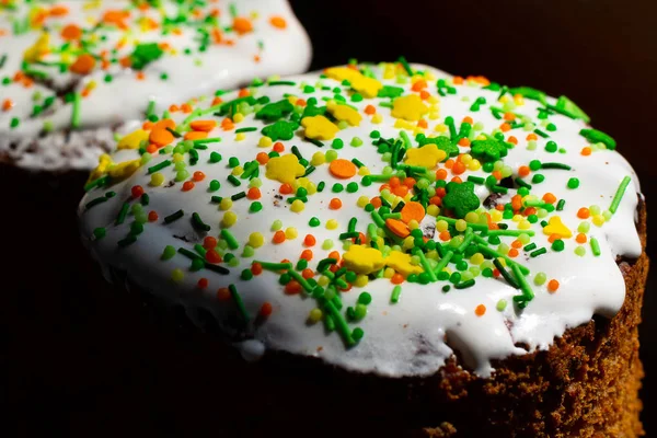 The top of the Easter cake, covered with white glaze and sprinkled with colored confectionery sprinkle close-up, black background in the background. Easter, a traditional Orthodox holiday in Ukraine