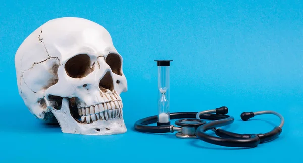 The flu virus epidemic. Human life and death from the virus. Human skull with phonendoscope and clock on a blue background. Front view, place for text, Copy space.