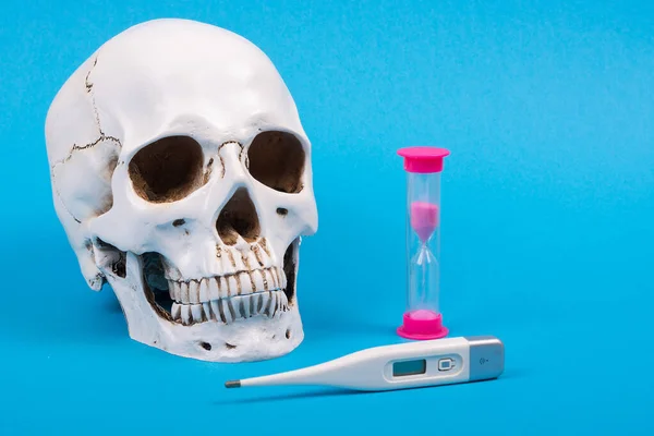 The epidemic of the virus. Human life and death from the virus. Human skull with a thermometer and a clock on a blue background. Front view, place for text, Copy space