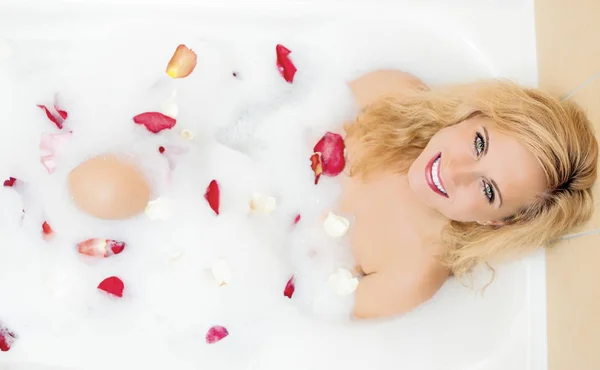 Spa Concepts and Ideas. Sensual Alluring Caucasian Blond Female in Foamy Bathtub Filled with Flowery Petals