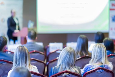 Beyaz ekran karşı seyirci önünde konuşan kadın ev sahibi