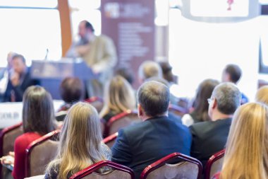 Beyaz ekran karşı seyirci önünde konuşan erkek ev sahibi