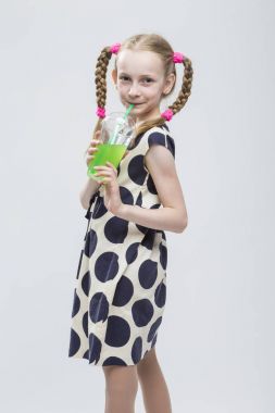 Portre sevimli beyaz küçük kız ile Pigtails poz bardak yeşil suyu ile Polka Dot elbiseli gülümseyen ve. Kamışla içme.