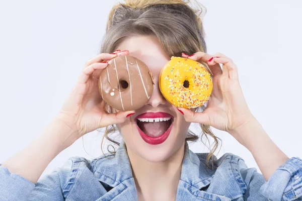 Beyaz sarışın kız gözleri önünde iki büyük çörek ile poz. Pozitif yüz ifadesi