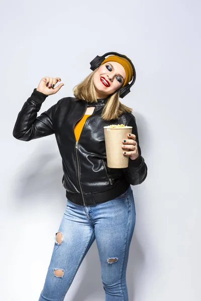 Portrait of Caucasian Female Blond Girl Holding A Bucket of Popcorn. Posing in Leather Jacket and Yellow Hat Against White.Vertical image