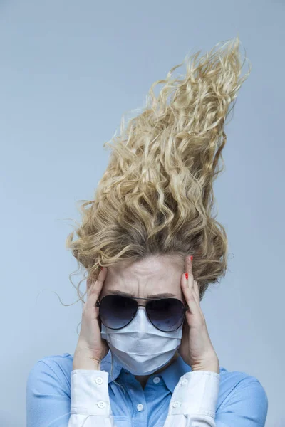 Portrait of Shocked Caucasian Woman With Lifted Hair. Wearing Flu Virus Mask For Viral Prevention With Black Glasses. Against Gray. Vertical image Orientation