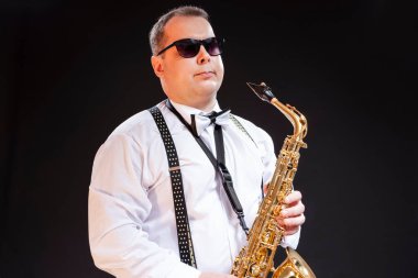 Beyaz Gömlekli Kafkasyalı Saksafoncu, Siyah Arkaplan Karşısında Güneş Gözlüklü Poz Veriyor. Yatay Bileşim