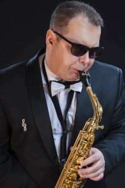 Müzik konseptleri. Siyah Arkaplana Karşı Güneş Gözlüklü Siyah Takımlı Tutkulu ve abartılı Saksafoncu Portresi. Dikey Resim Yönlendirmesi