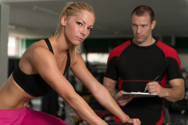 Donna treno bicicletta sulla macchina con personal trainer — Foto Stock