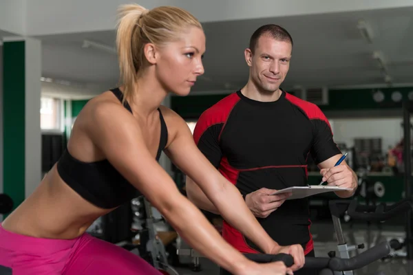 Mulher trem bicicleta na máquina com personal traininer — Fotografia de Stock